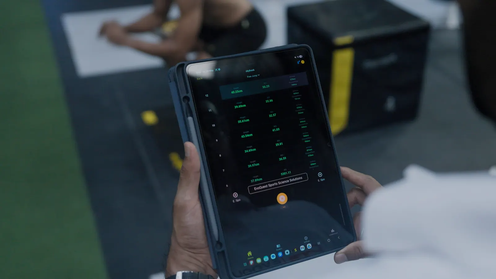 EvoQuest practitioner holding a tablet of live jump results while an athlete tests in the background