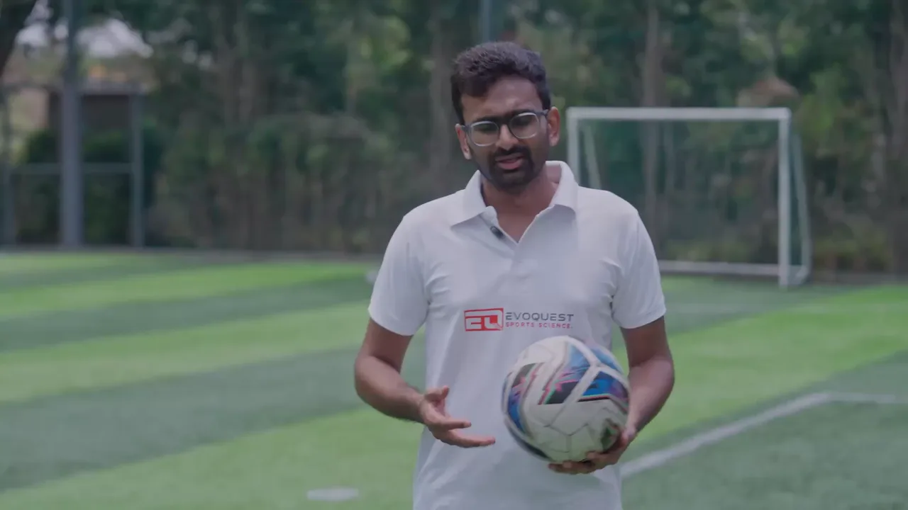 EvoQuest coach holding a football on the pitch, about to explain GPS tracking